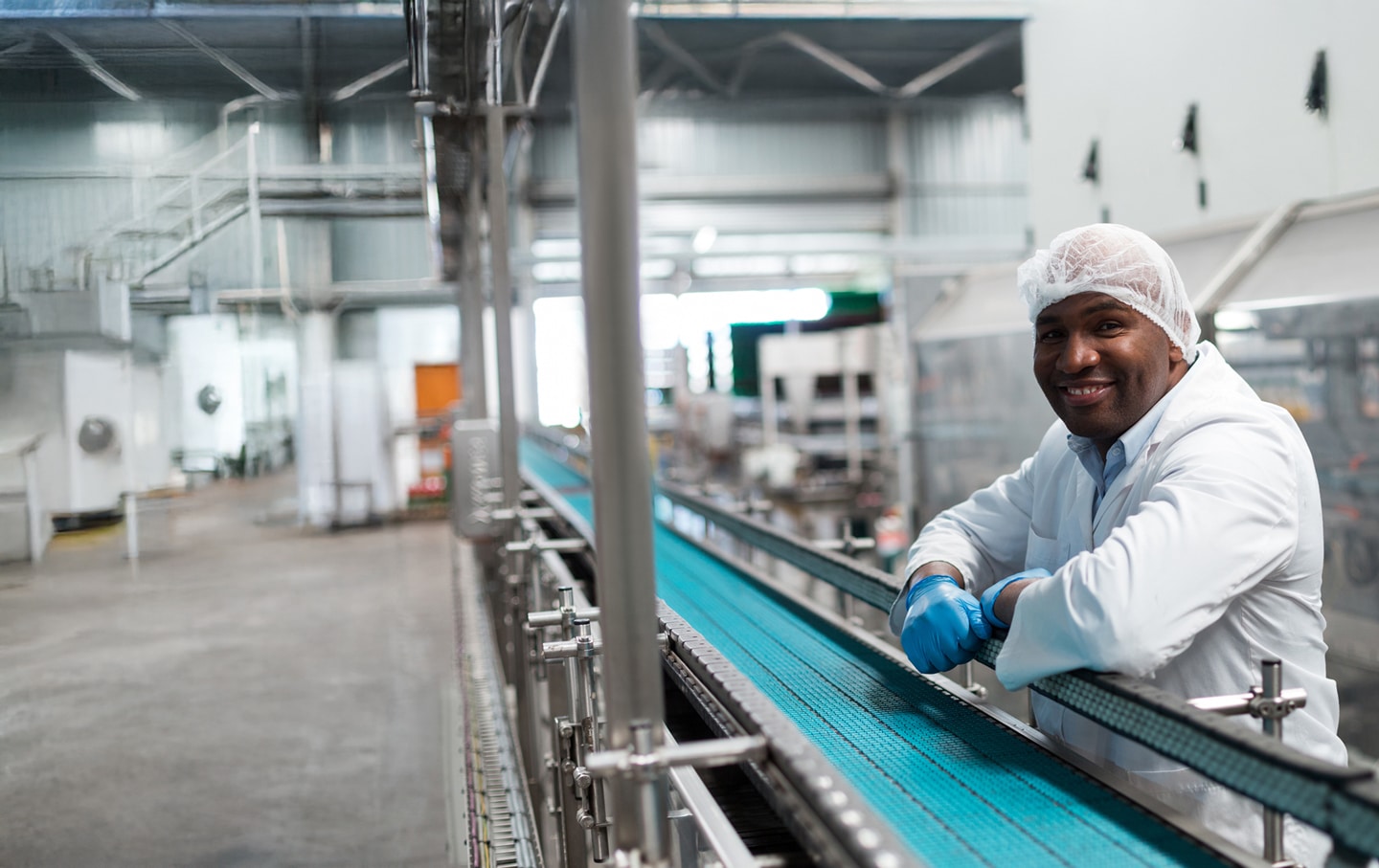 http://Smiling%20food%20factory%20worker%20in%20protective%20clothing%20standing%20beside%20a%20clean%20production%20line%20in%20a%20modern%20food%20processing%20facility.
