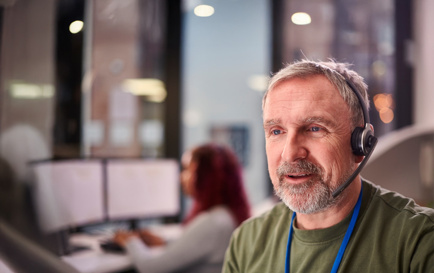 http://Mature%20customer%20service%20agent%20wearing%20a%20headset,%20speaking%20with%20a%20client%20in%20a%20modern%20office%20environment%20with%20multiple%20computer%20screens%20in%20the%20background.