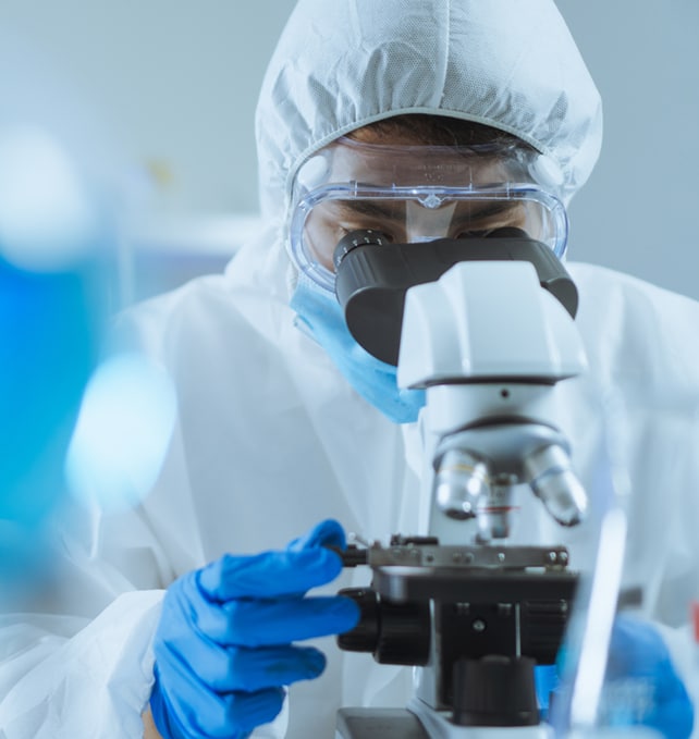 Scientist in full protective lab gear using a microscope for analysis and quality control in a laboratory setting.
